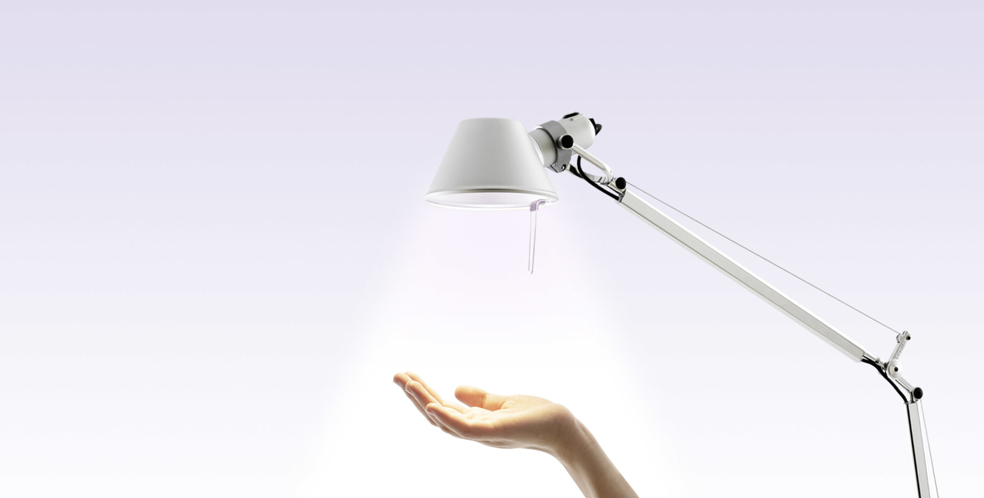 Artemide Tolomeo table lamp in white, with articulated arm, casting warm light onto an open hand below.
