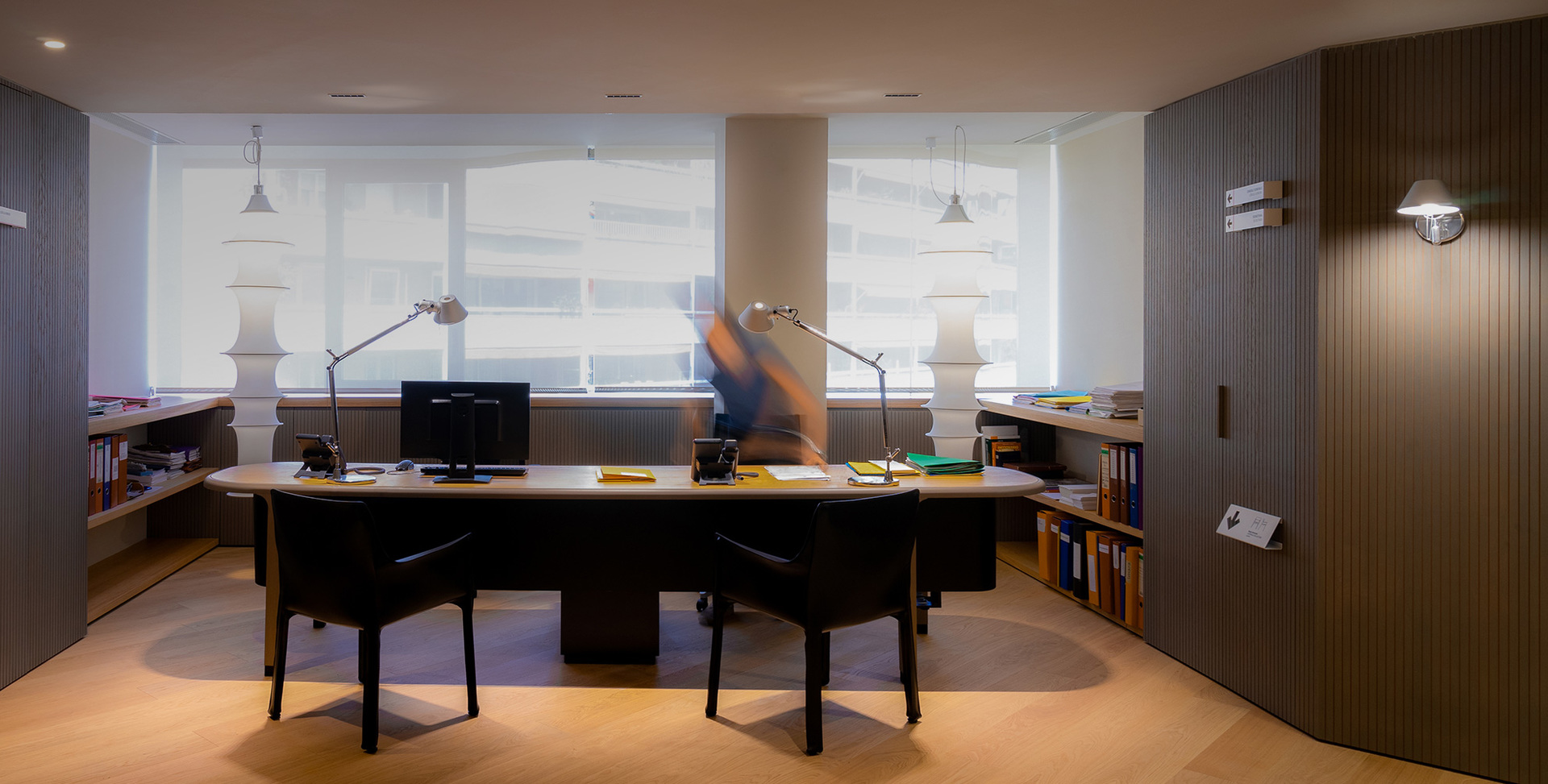 Modern office with curved desk, two Artemide Tolomeo desk lamps, pendant lights, and a wall-mounted lamp on fluted panel.