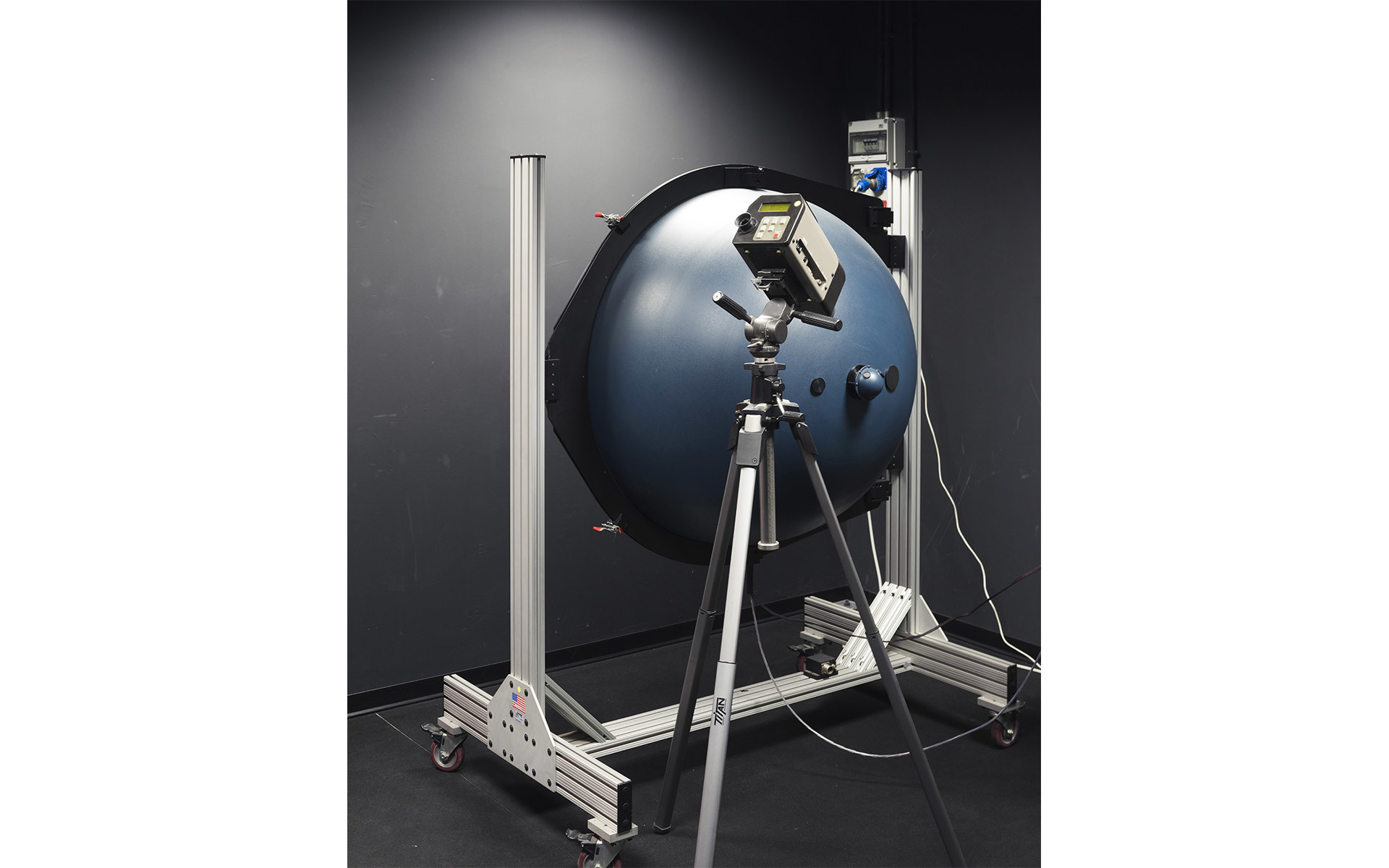 Integrating sphere photometer on a tripod used for measuring luminous flux and optical performance of lighting fixtures in a lab.