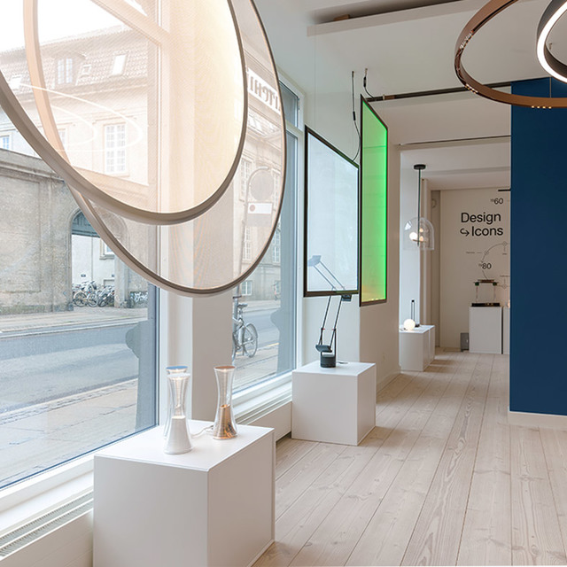 Artemide showroom displaying Design Icons collection: circular pendant rings overhead, table lamps on white plinths, colorful backlit panels.