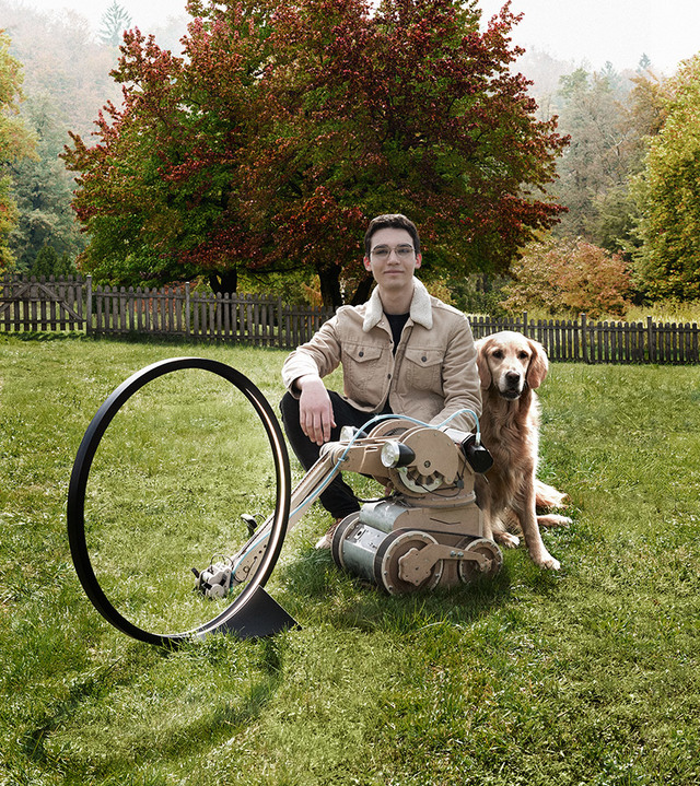 Young man sitting on grass with a golden retriever beside a circular floor lamp with a ring-shaped shade, autumn trees in background