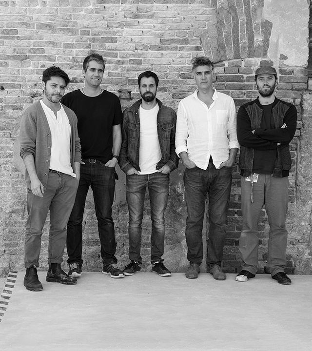 Five men standing together against a brick wall, posing for a group portrait in casual attire.
