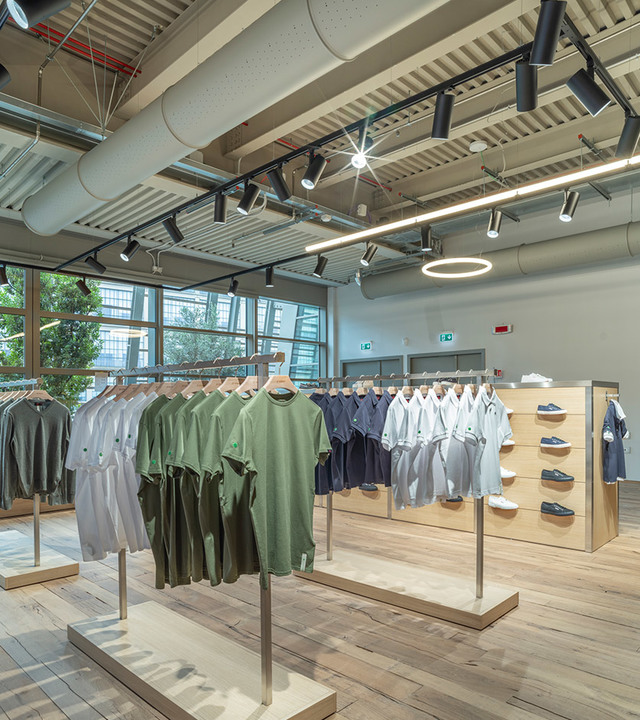 Clothing store interior with Artemide track spotlights and circular pendant illuminating garment displays on light wood fixtures.