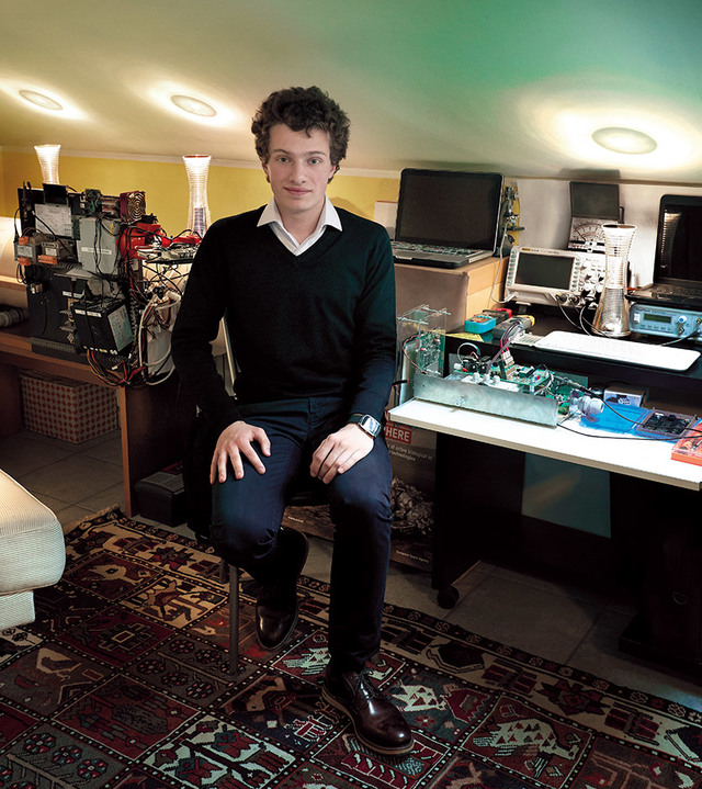 Young man seated in a tech workspace with Artemide ceiling lights illuminating the room, surrounded by electronic equipment.