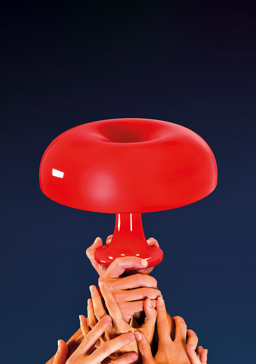 Multiple hands reaching up together to hold the Artemide Nessino table lamp with its iconic red mushroom-shaped shade.