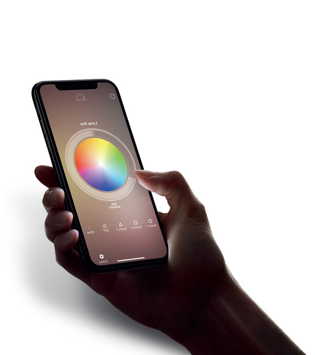 Hand holding a smartphone displaying the Artemide app with a color wheel interface to control smart lighting settings.