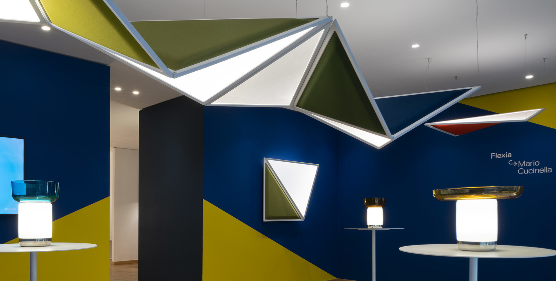 Artemide Flexia by Mario Cucinella: geometric ceiling and wall panels with integrated lighting, paired with table lamps in a showroom display