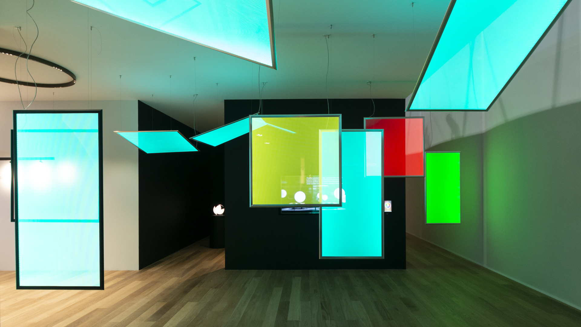 Artemide showroom with vibrant cyan, green, and red luminous flat panels as ceiling and pendant lights illuminating a dark interior.