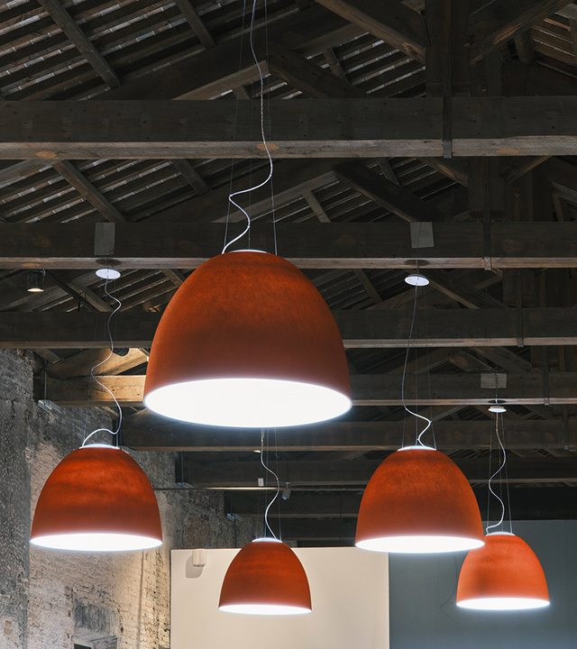 Five Artemide Nur Mini pendant lamps with terracotta-colored diffusers emitting warm white light, suspended from a rustic wooden beam ceiling.