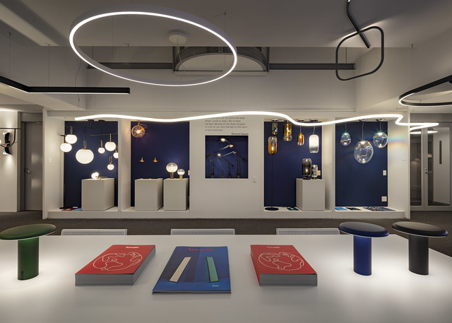Artemide showroom displaying pendant and ceiling lights, including large circular LED rings and colorful glass pendants on navy blue backdrop.