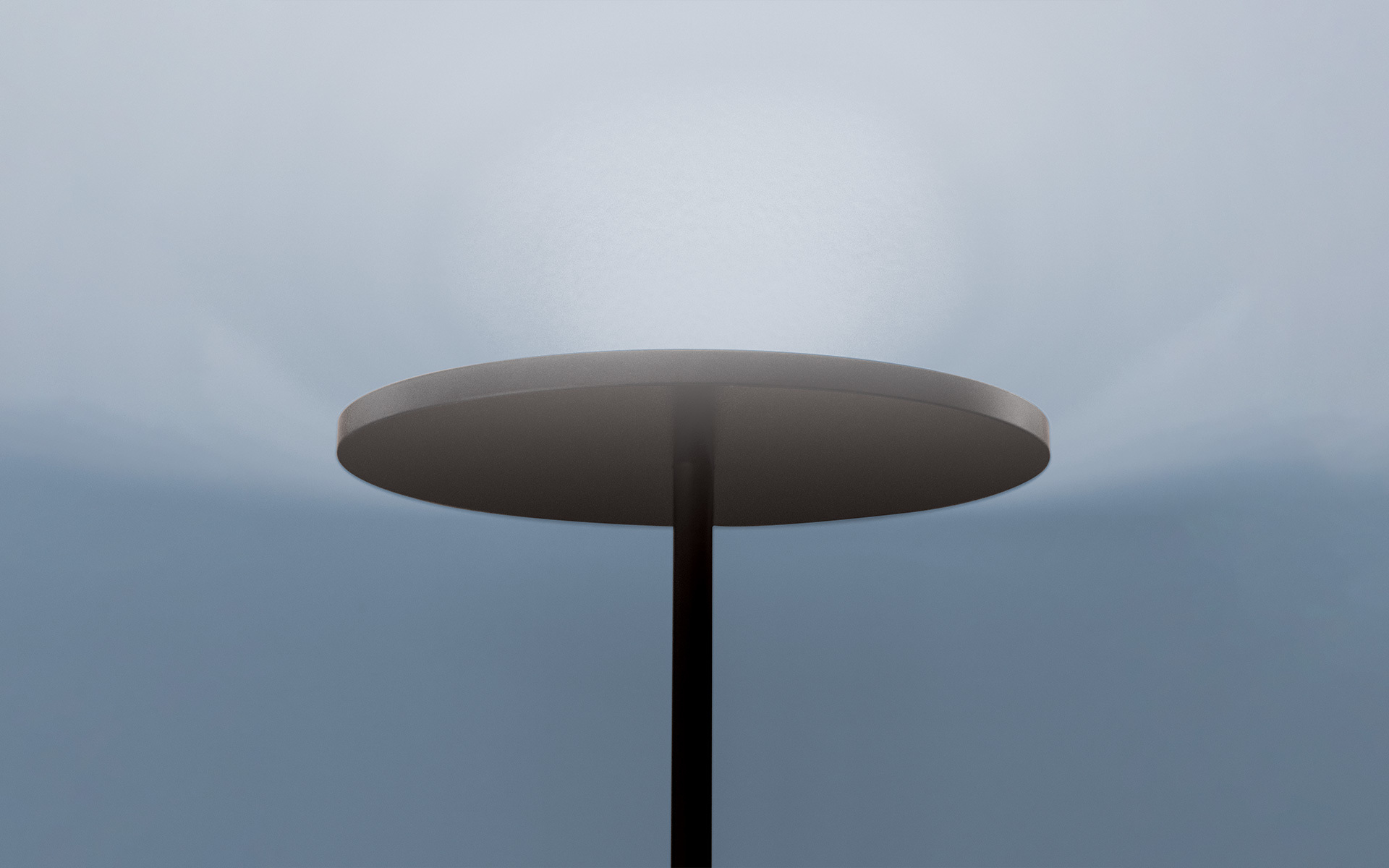 Artemide floor lamp with dark circular disc shade on slim black stem, emitting soft upward glow against overcast sky