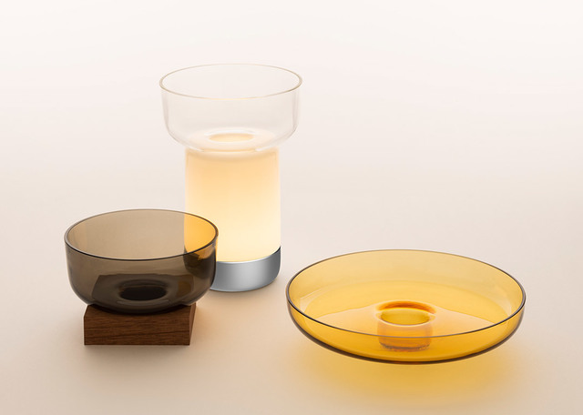 Artemide table lamp collection: smoky glass bowl on wood base, glowing cylindrical lamp, and amber glass dish with central holder