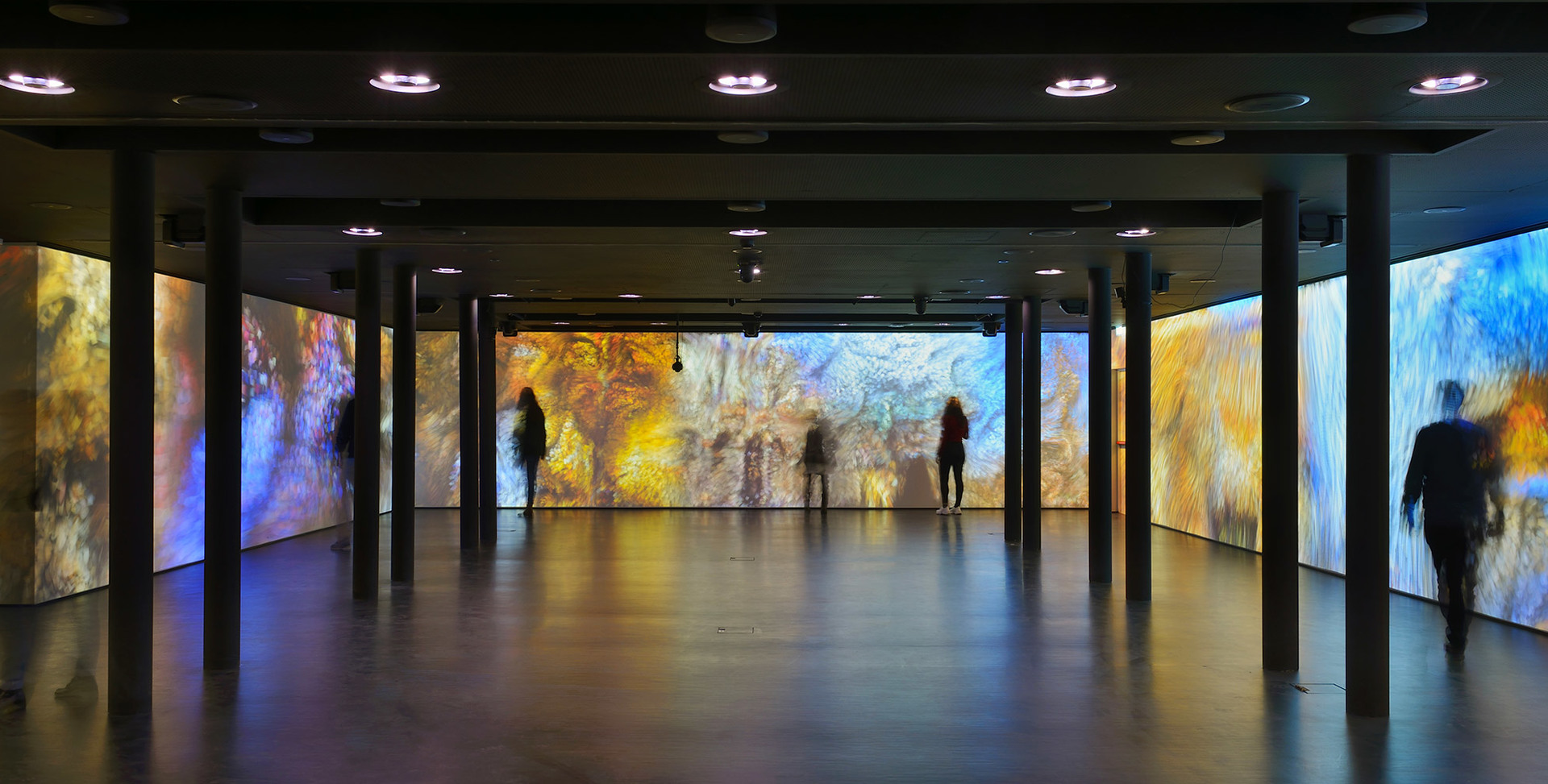 Immersive art installation with colorful projected walls, visitors silhouetted, lit by Artemide recessed ceiling spotlights in a dark gallery