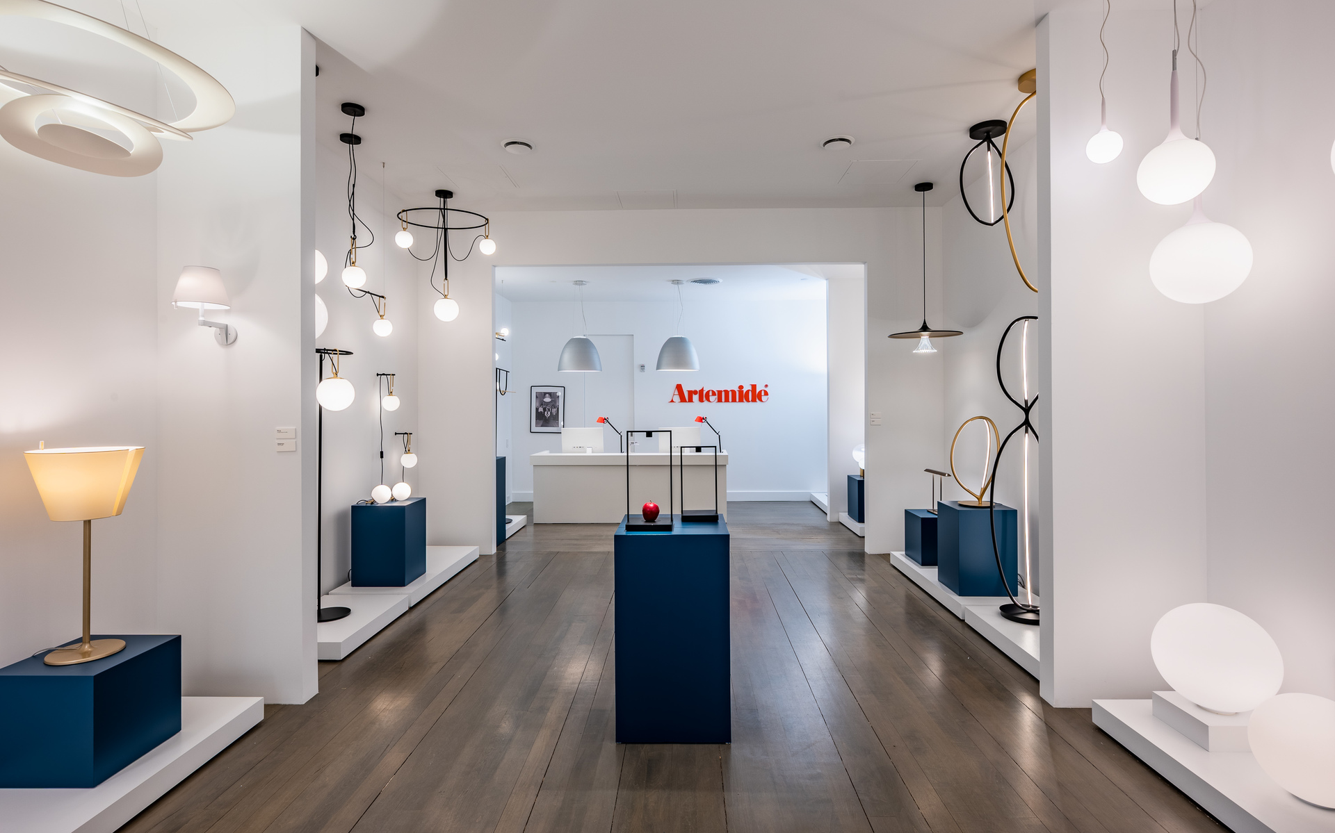 Artemide showroom displaying diverse lighting collection: pendant, wall, and table lamps with white glass globes and circular designs on dark wood floor