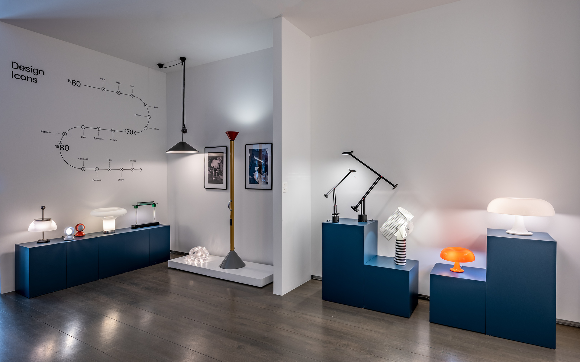 Artemide Design Icons exhibition showcasing iconic lamps on blue plinths, including table, floor, and pendant lights across decades.