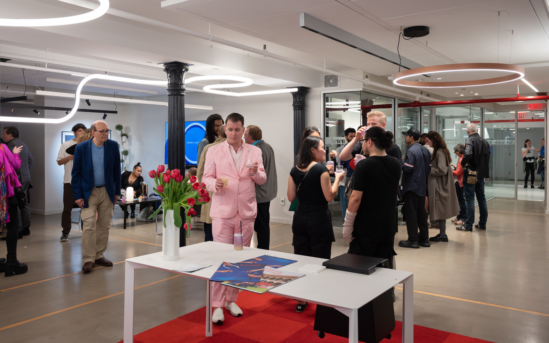 Artemide lighting event: guests mingle in a modern space featuring white sinuous and circular red pendant lights overhead.