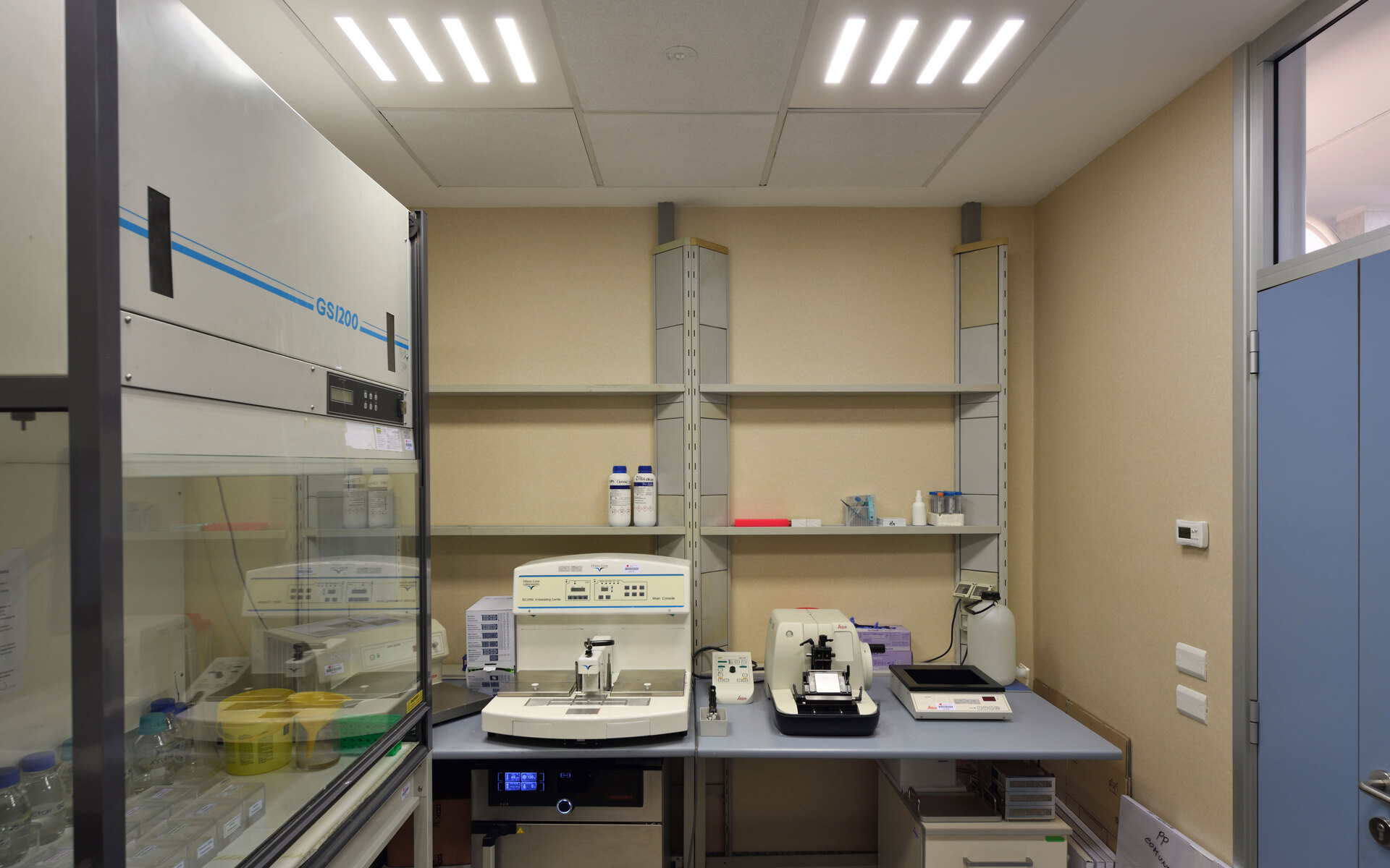 Laboratory workspace illuminated by Artemide recessed LED panel lights on ceiling, with scientific instruments on workbench and shelving units.