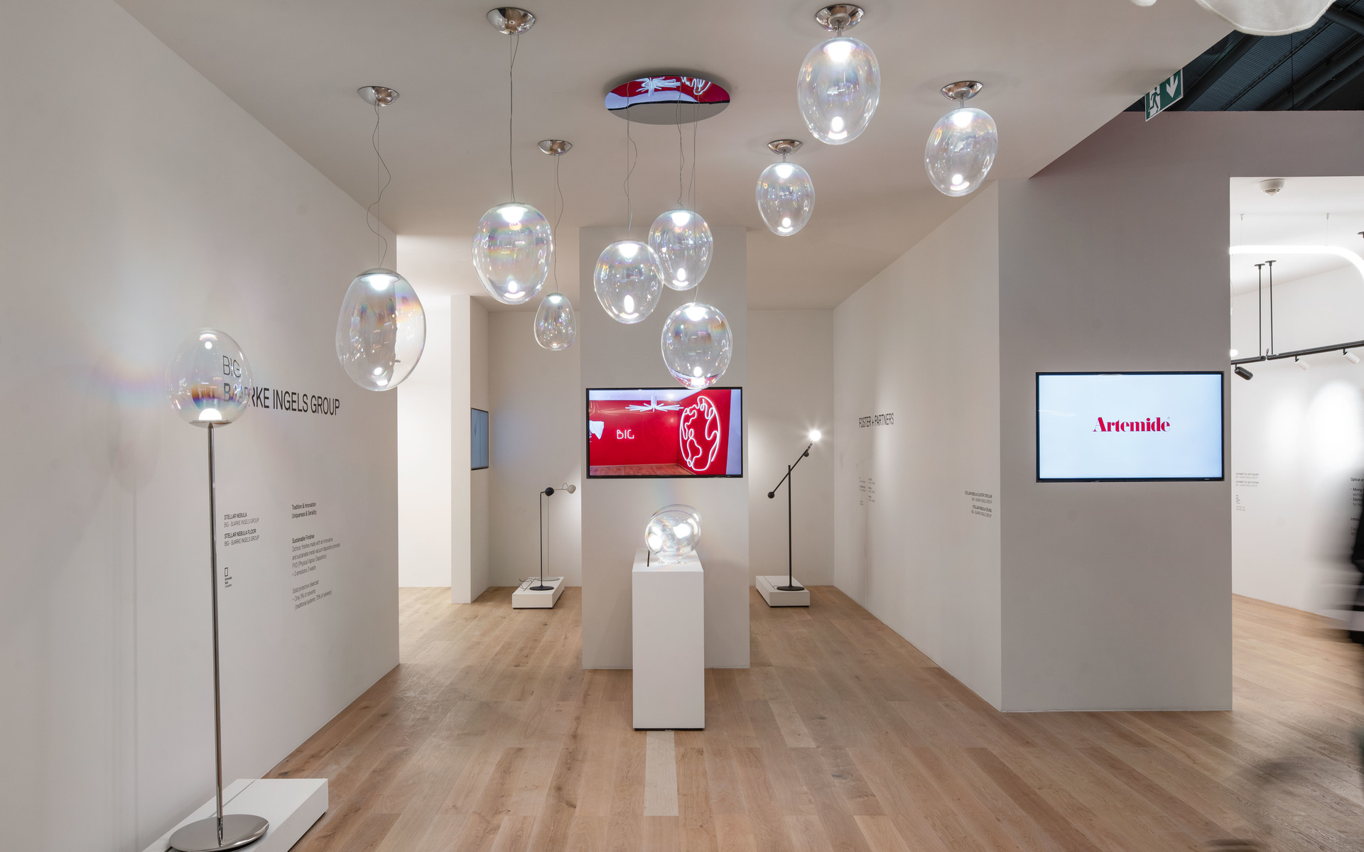Artemide showroom with multiple transparent glass bubble pendant lights, floor lamps, and display pedestals in a bright white space.