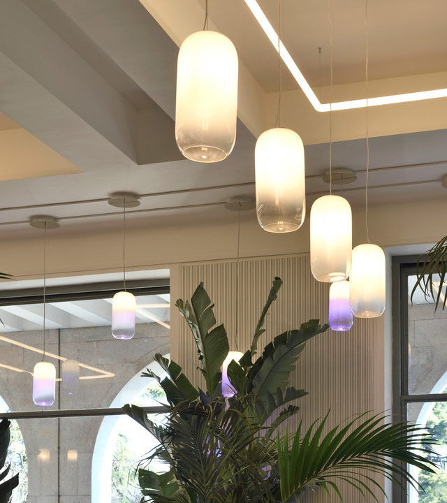 Artemide Gople pendant lamps in white blown glass with purple base glow, suspended over tropical indoor plants in a modern interior