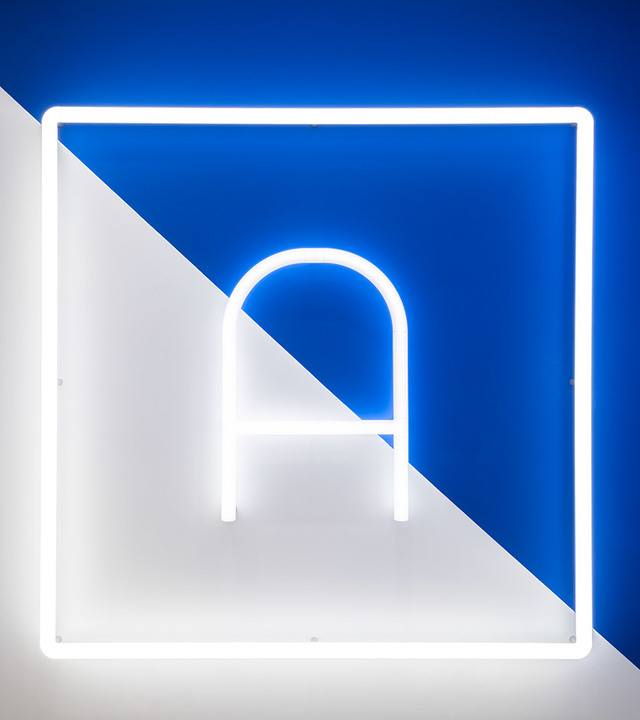 Artemide logo in white neon light forming letter A with arch, framed by glowing square, against blue and white diagonal background