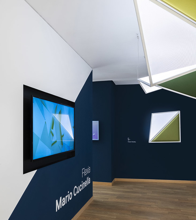 Artemide Flexia lamp by Mario Cucinella displayed in a dark blue exhibition space with geometric ceiling installation.