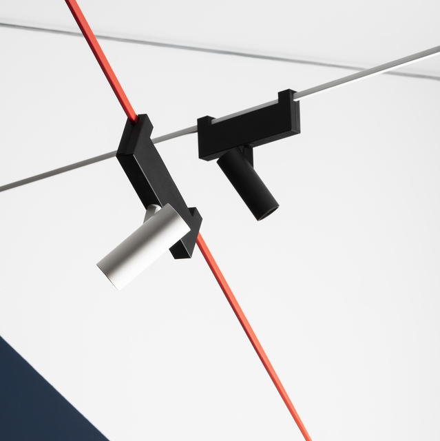 Two adjustable track spotlights in black and white mounted on a cable system with a red power cord on a white ceiling