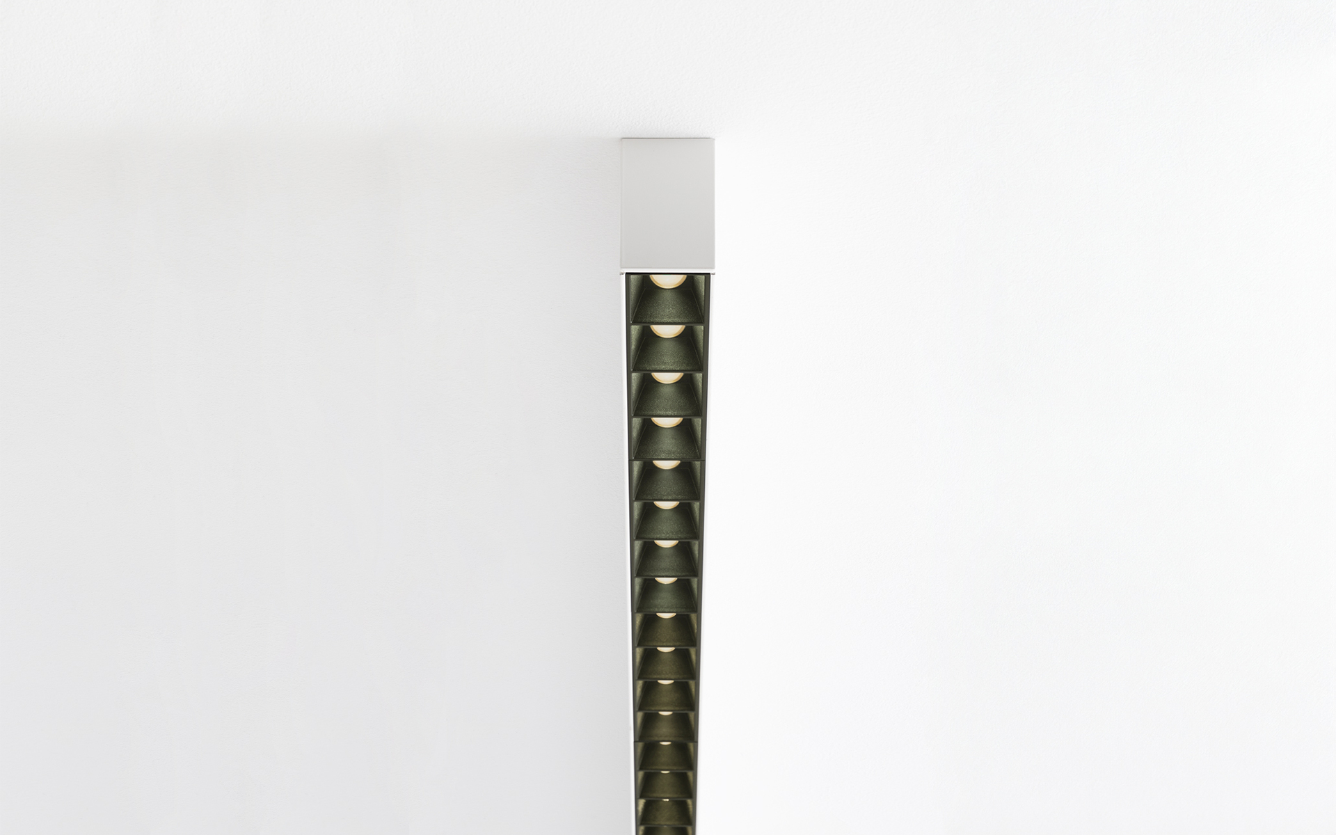 Vertical dark bronze linear LED fixture with honeycomb anti-glare cells, ceiling-mounted, emitting downward directional light