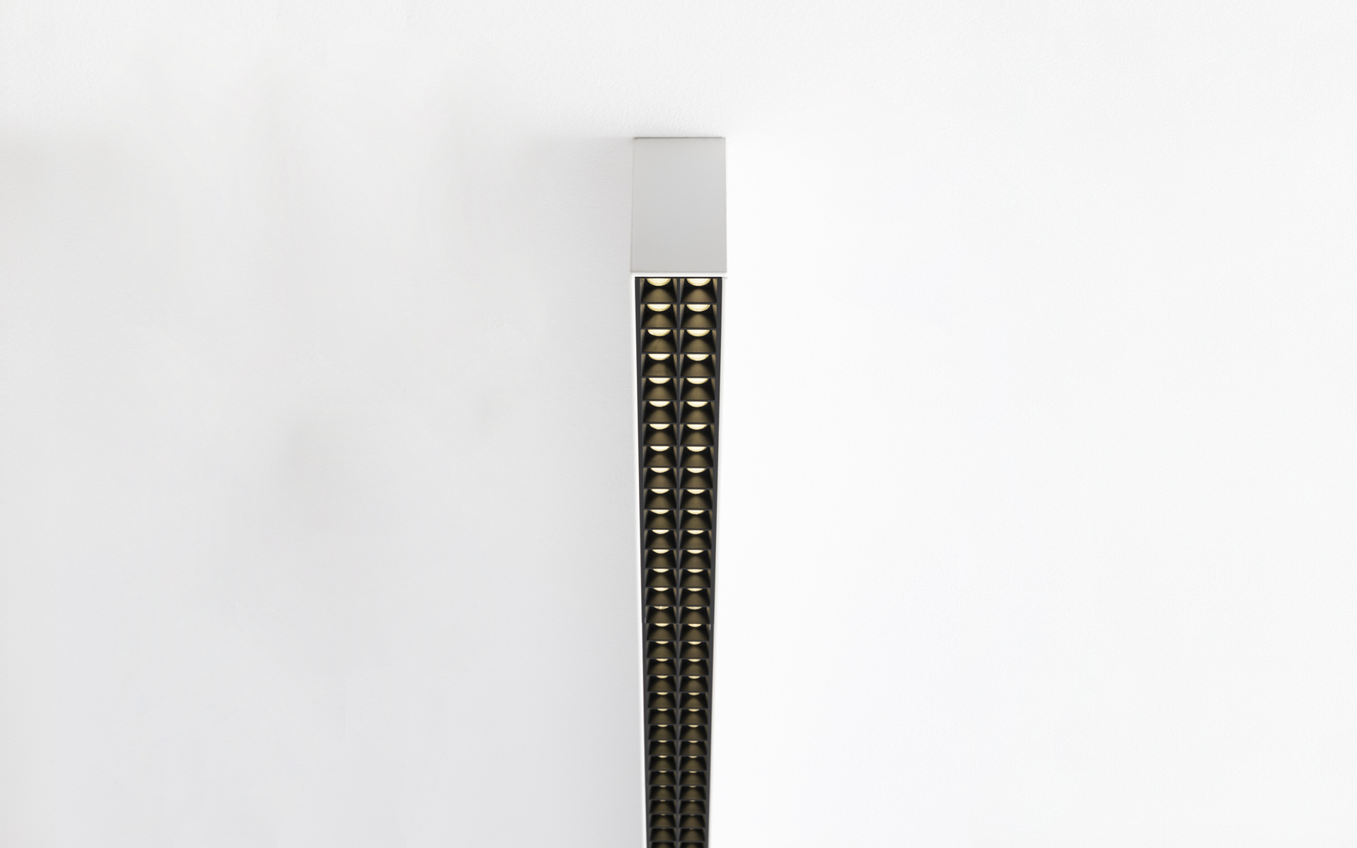 Vertical wall lamp with slim white body and double row of small golden LED lenses on dark strip, mounted flush to wall