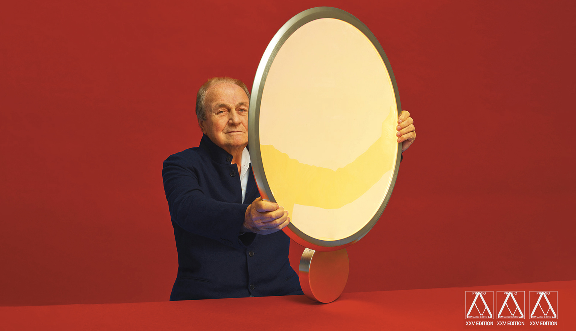 Designer holding the Artemide Fato lamp, an oval LED luminaire with silver rim and warm light, against a red background.
