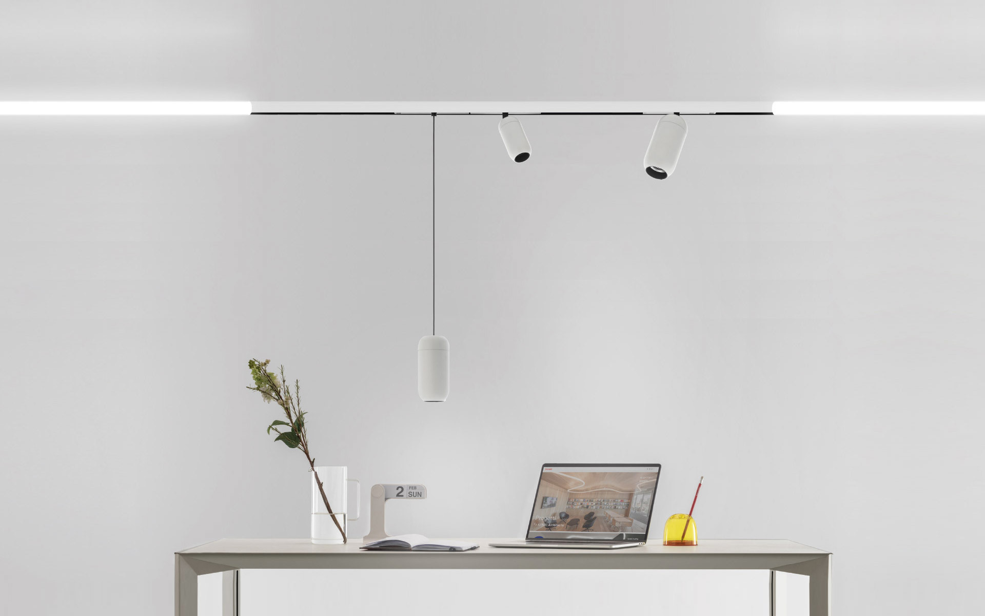 Artemide track lighting system with linear LED bar, two adjustable spotlights, and a cylindrical pendant lamp above a minimalist desk.