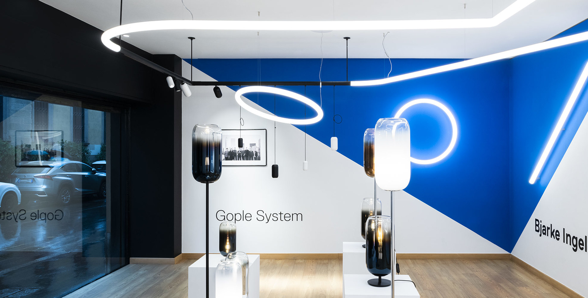 Artemide showroom featuring Gople System floor lamps with smoked glass shades and circular pendant lights on a blue and white wall.