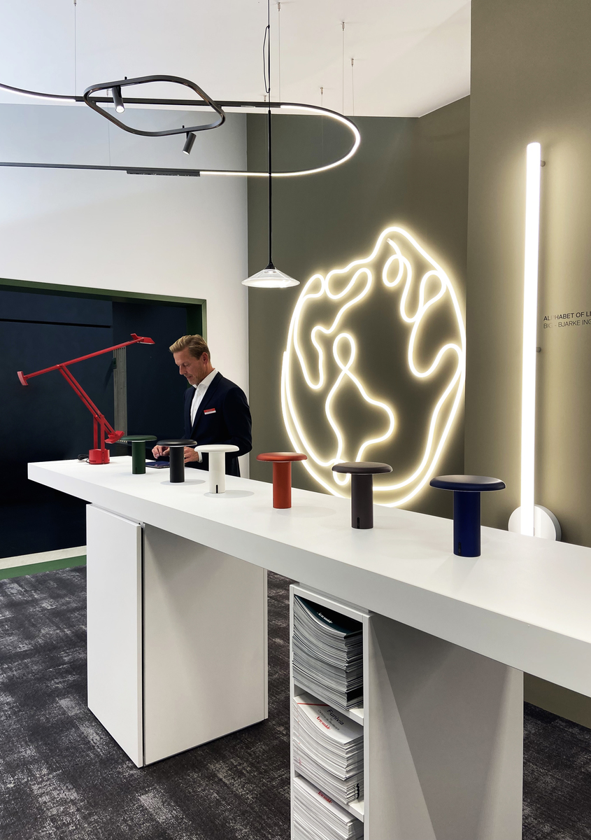 Artemide showroom display with colorful Tagora table lamps, a red Tolomeo desk lamp, circular pendant, and glowing globe wall installation.