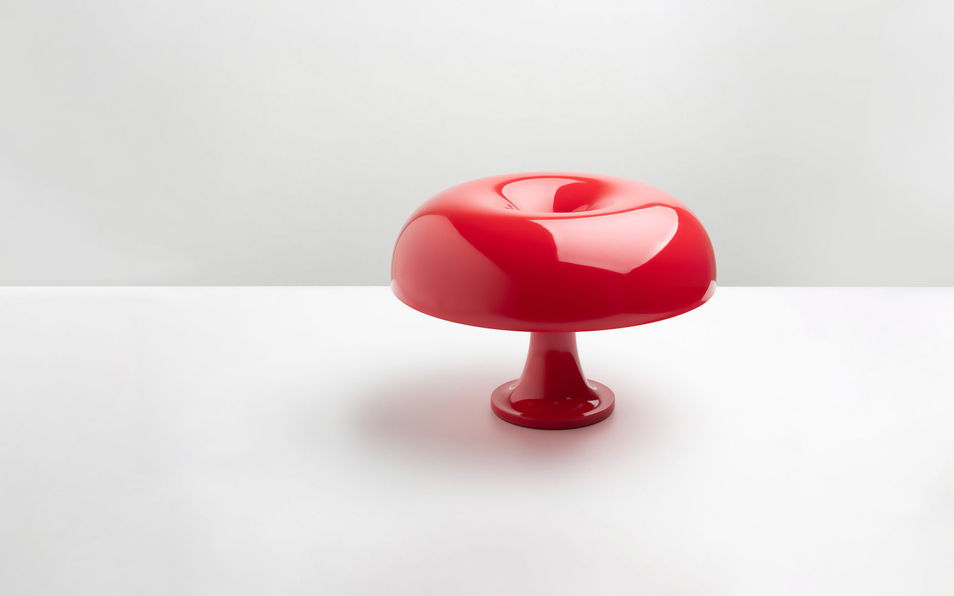 Artemide Nessino table lamp in glossy red, featuring a mushroom-shaped shade on a slender pedestal base