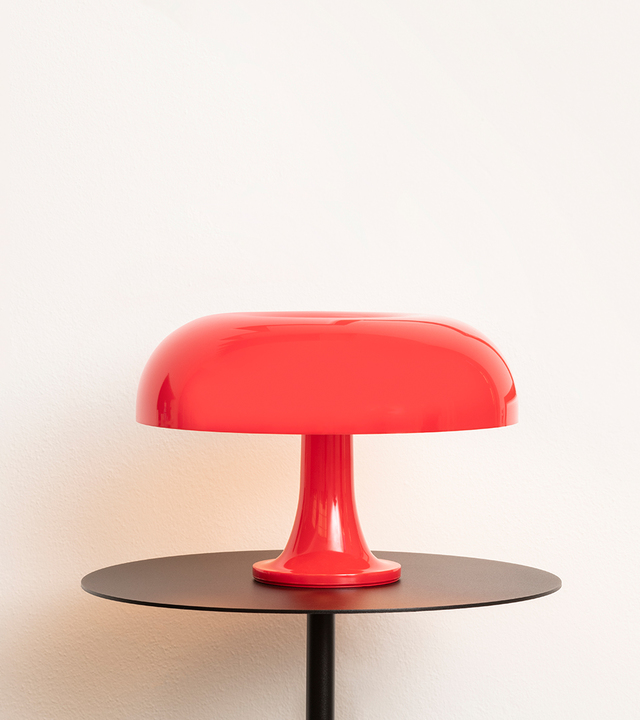 Artemide Nessino table lamp in red, featuring iconic mushroom-shaped shade on a pedestal base, placed on a dark round table