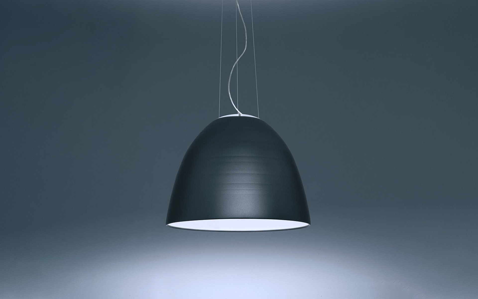 Artemide dark anthracite dome-shaped pendant lamp with white inner diffuser, suspended by thin cables, casting downward light.
