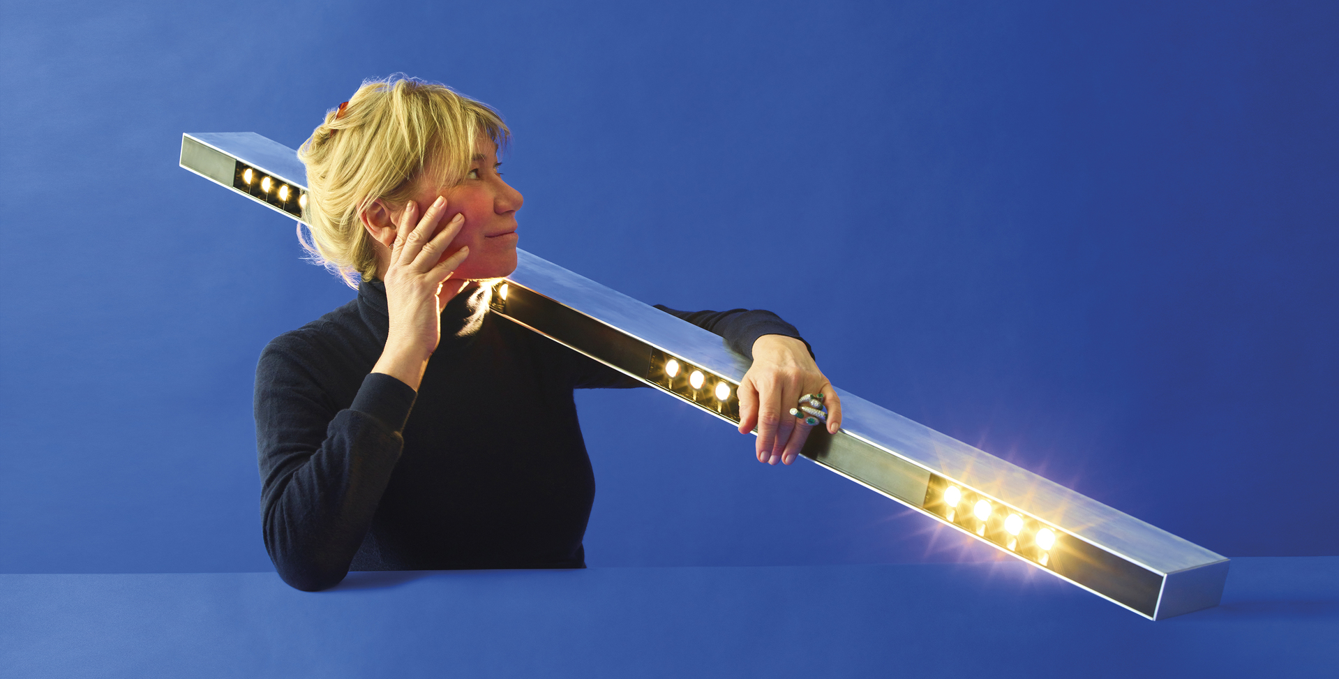 Woman holding a long rectangular LED bar light with warm white LEDs emitting light, showcasing Artemide linear lighting design.