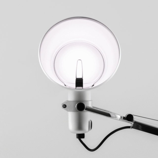 Close-up of Artemide Tolomeo lamp head: white conical shade with adjustment pin, pivoting joint, and articulated chrome arm with cable