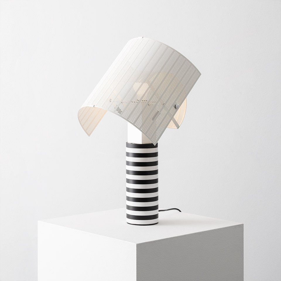 Artemide Shogun table lamp with black-and-white striped cylindrical base and tilted ribbed white shade, displayed on a white pedestal