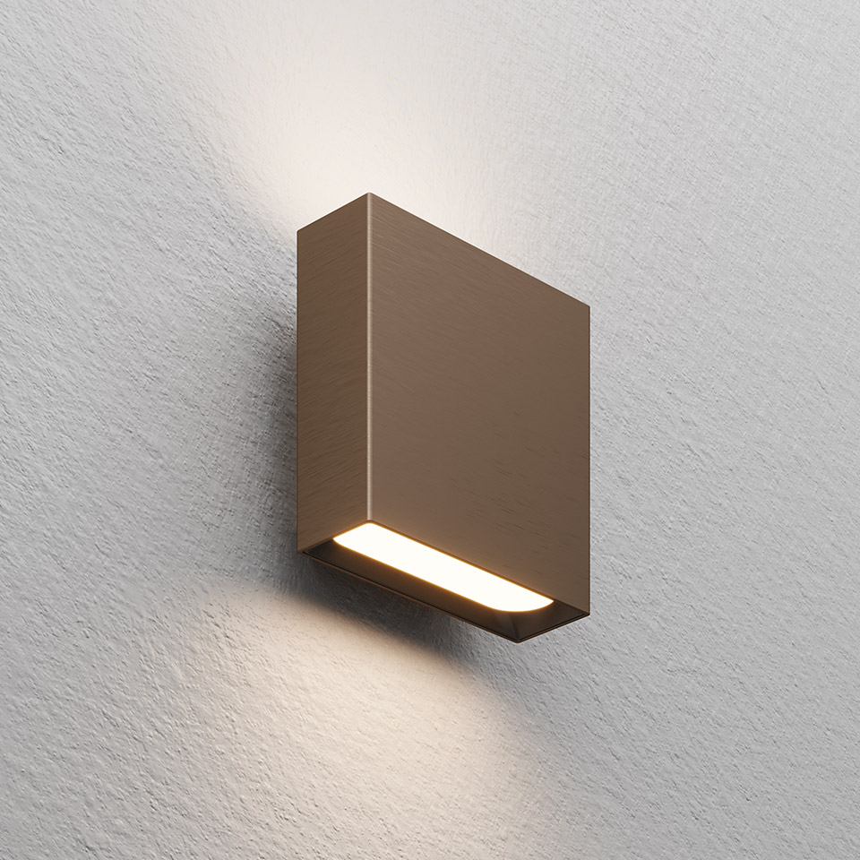 Agathe wall lamp by Artemide: compact square bronze body with bottom LED strip emitting warm upward and downward light