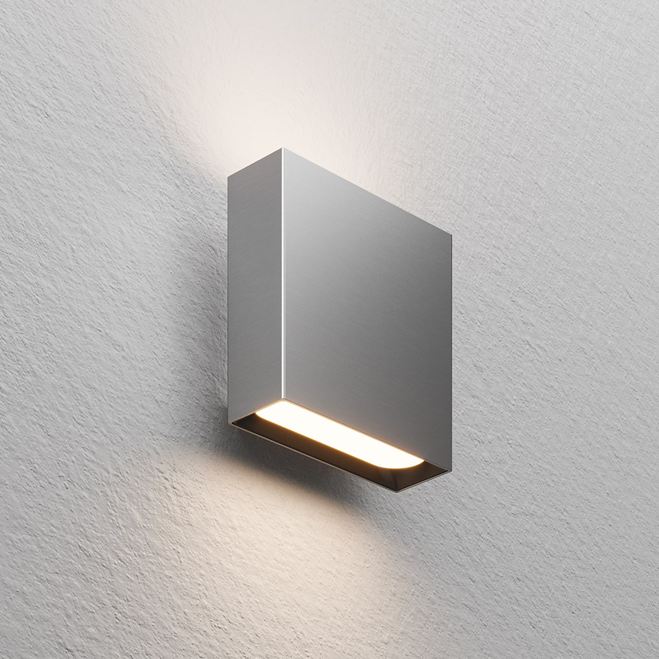 Agathe wall light by Artemide: compact rectangular grey fixture with bottom LED strip emitting warm light downward on textured wall