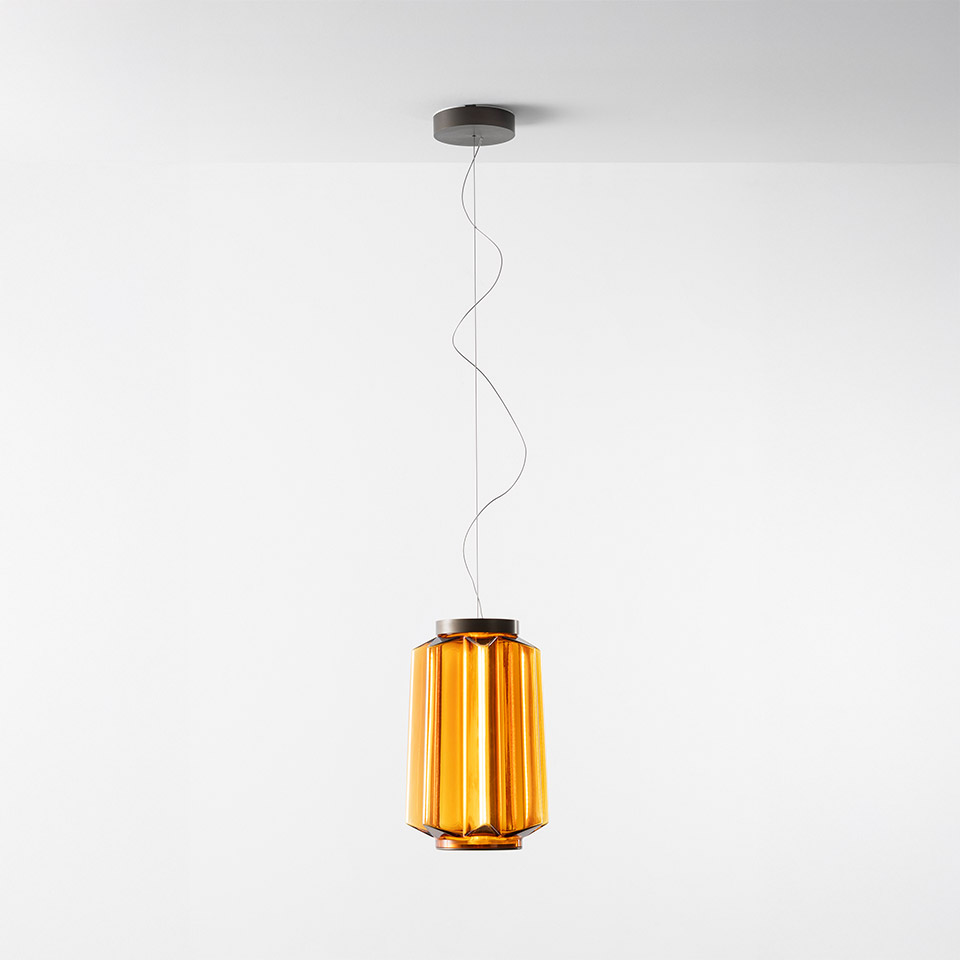 Artemide Auralia pendant lamp with amber glass diffuser featuring vertical ribbed panels, suspended by a thin cable from a grey ceiling rose