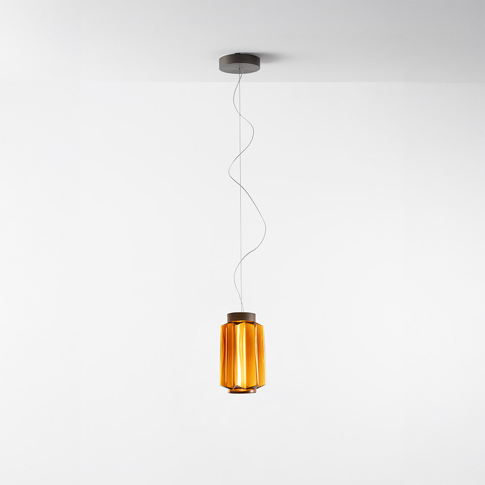 Artemide Auralia pendant lamp with amber cylindrical ribbed glass diffuser and dark metal top, suspended by a thin cable