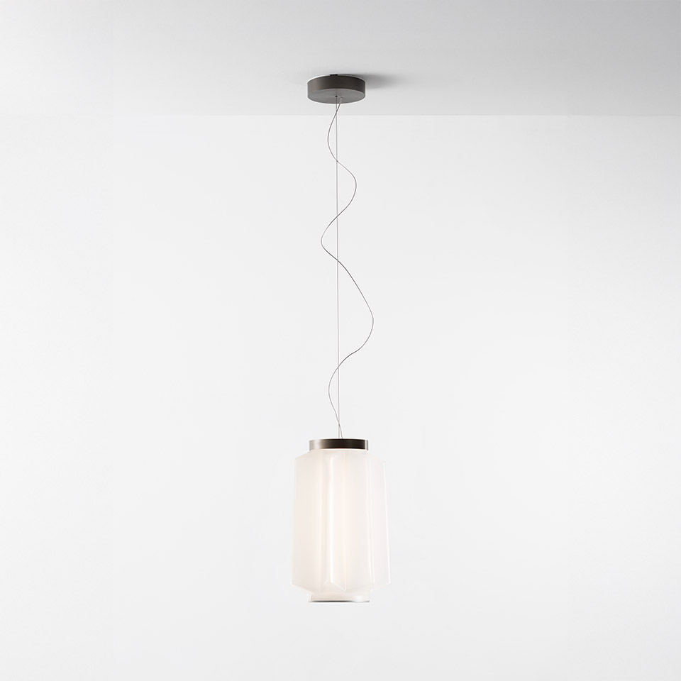 Artemide Auralia pendant lamp: cylindrical opaline glass diffuser with dark metal top cap, suspended by a wavy cable from a ceiling rose