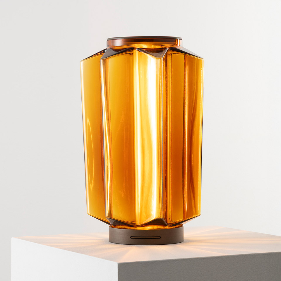 Auralia table lamp by Artemide: faceted amber glass diffuser with warm glow, bronze metal base with rechargeable battery