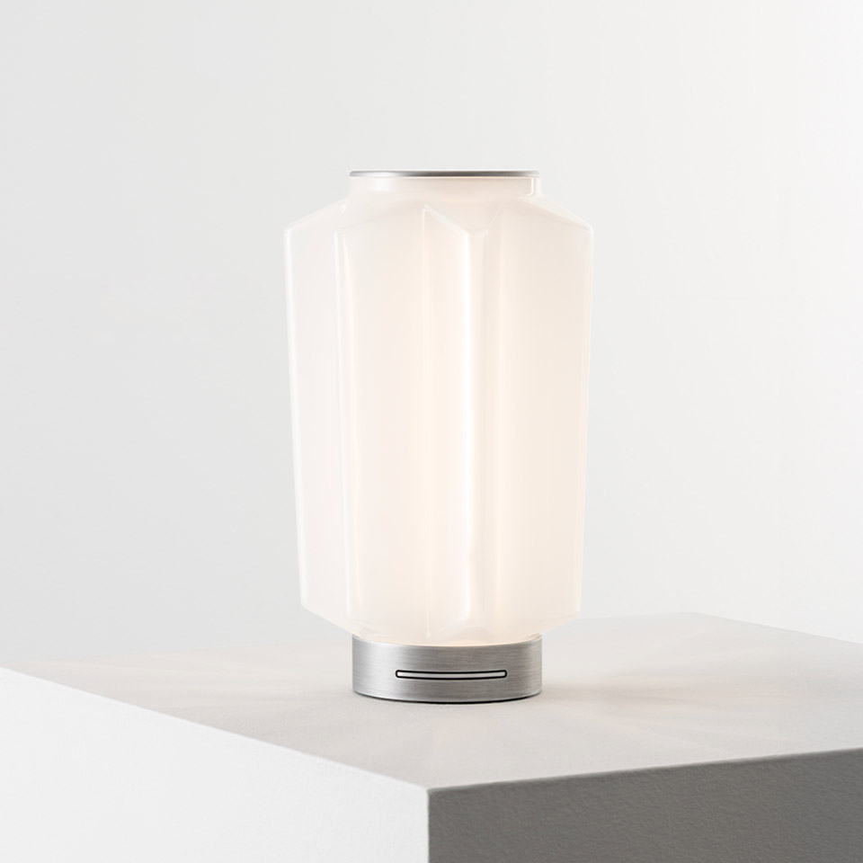 Artemide Auralia table lamp with opal white glass diffuser and brushed aluminum base, glowing softly on a surface