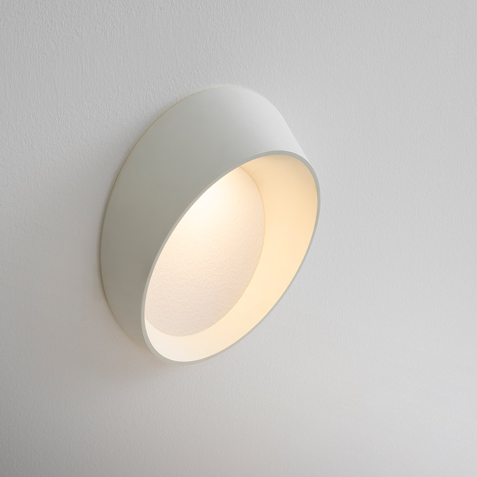 Artemide Cleomede wall lamp: white tilted cylindrical shade with warm LED light, mounted flush on a white wall