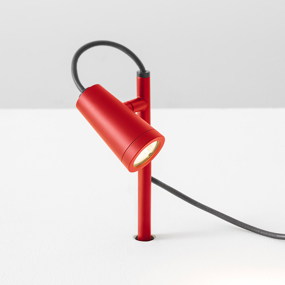 Artemide Conus table spotlight in red, featuring a cylindrical adjustable head on a slim stem with a dark grey cable