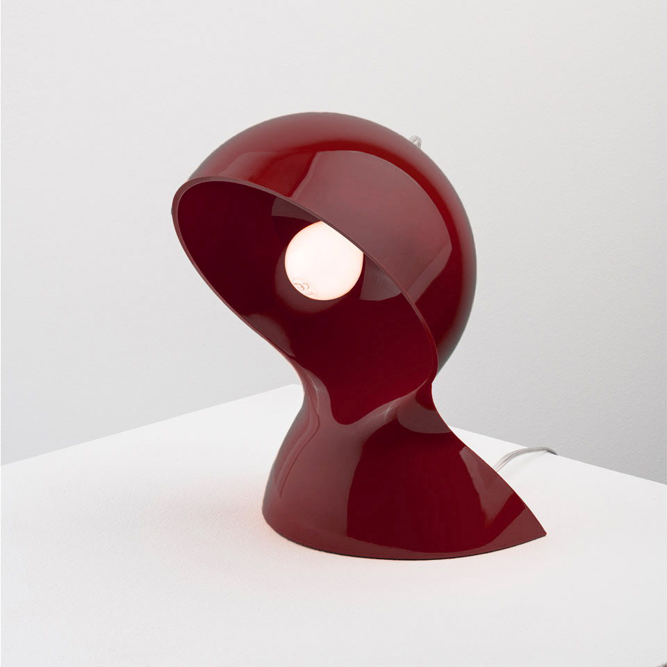 Artemide Dalù table lamp in glossy dark red, featuring a sculptural curved shell shape with exposed bulb, placed on a white surface