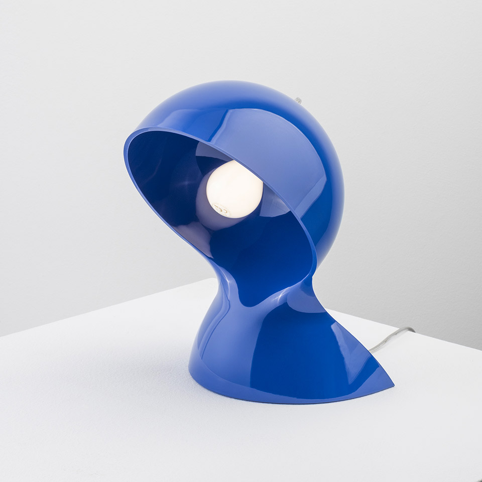 Artemide Dalù table lamp in glossy blue, featuring a sculptural helmet-shaped shade with exposed bulb, placed on a white surface