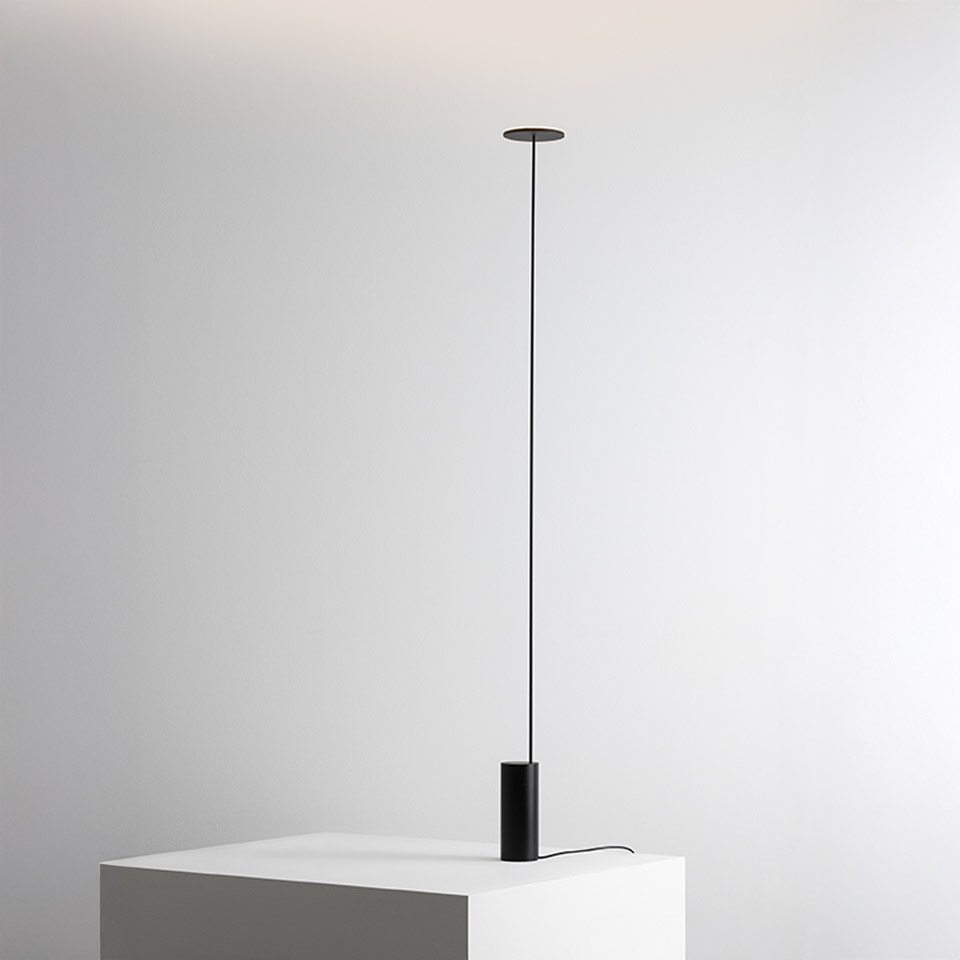Artemide Helgoland floor lamp: ultra-thin black stem connecting ceiling canopy to cylindrical base on white surface